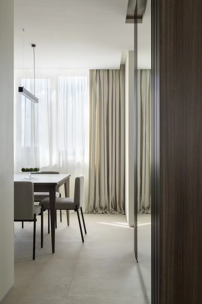 A contemporary dining area with a table and chairs, sheer white curtains, and pleated light beige blackout curtains.