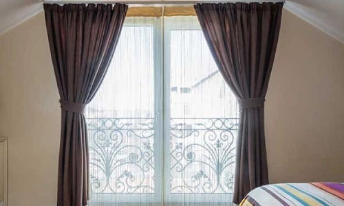 Attic bedroom with light wood flooring and a balcony door covered by sheer and blackout curtains in District One.