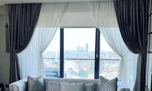 Gray, velvet-look blackout curtain dubai are tied back to reveal a sheer center panel and a stunning high-rise cityscape view.