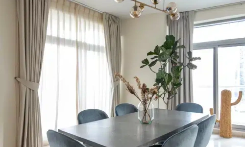 Modern dining room with a square table, blue velvet chairs, and light taupe blackout curtains suitable for a luxury apartment in District One.