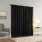 A pair of luxurious, floor-length velvet blackout curtains in black, hung on a dark rod against a light gray wall, creating a dramatic