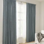 The outer layer consists of heavy, textured, blue-grey cotton blackout curtains hung with a gathered or pinch pleat style from a brushed metal rod.