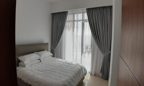 blackout curtains are tied back to reveal sheer white inner curtains, allowing natural light to fill the room.