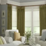 A bright living room featuring layered living room blackout curtains in a sage green lattice pattern paired with white cellular shades.