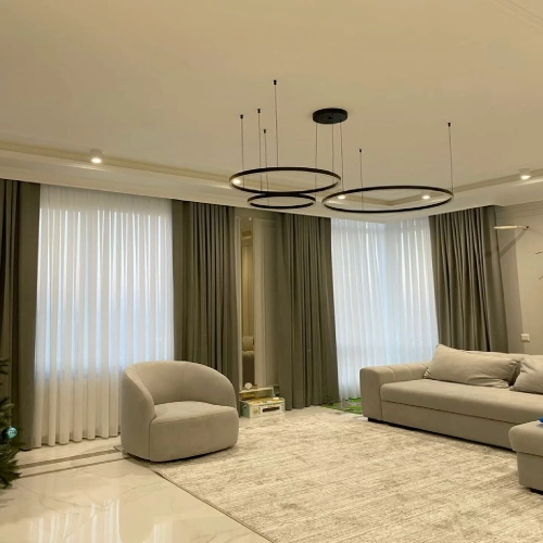 A modern living room featuring elegant living room blackout curtains in a muted olive green, layered over sheer white drapes.