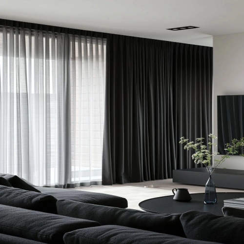 A modern, minimalist living room featuring layered window treatments with sheer white panels and charcoal gray blackout curtains that extend from floor to ceiling.