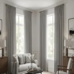 Classic Pleated living room blackout curtains in a soft grey fabric hang from floor to ceiling over two large windows in a bright