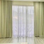 motorized living room blackout curtains and sheer drapes installed on a large window wall over light wood flooring.