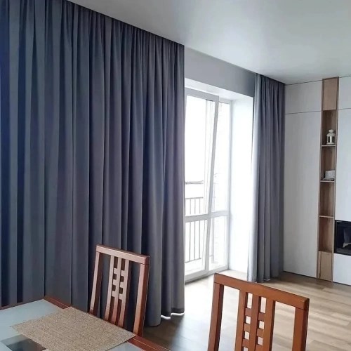 A bright dining area featuring floor-to-ceiling dining area blackout curtains in a sleek slate gray, partially drawn to reveal a glass balcony door.