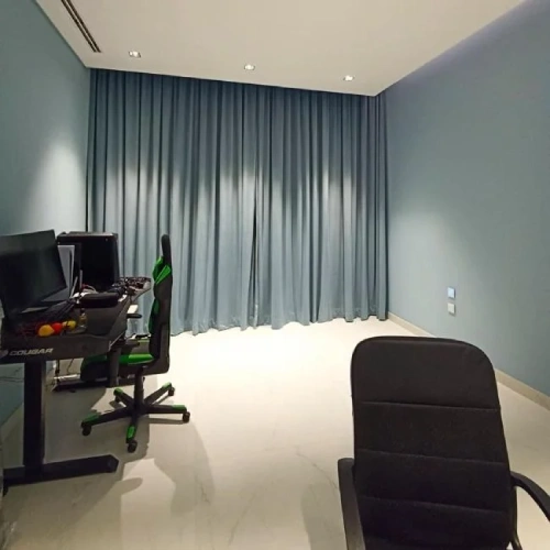 An empty home office featuring floor-to-ceiling home office blackout curtains in a muted blue, providing full light control for a gaming setup.
