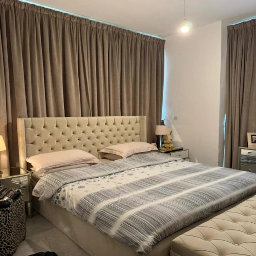 Luxurious master bedroom with floor-to-ceiling taupe blackout curtains in Dubai serving as a soft backdrop for a tufted beige headboard.