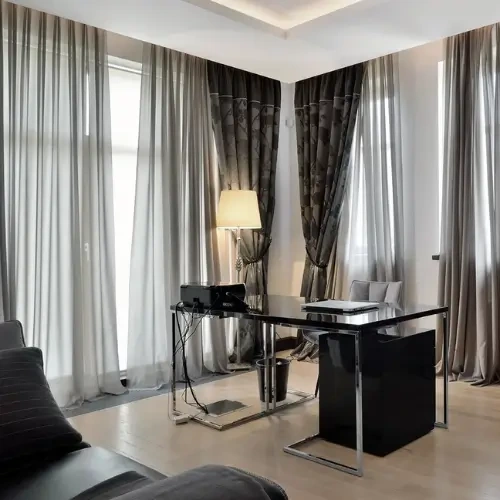 A modern home office featuring floor-to-ceiling Cotton-Blend Blackout curtains in a deep charcoal grey with a subtle pattern