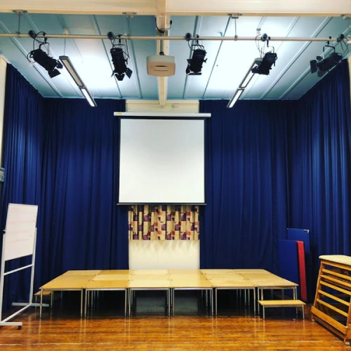 A university lecture hall or small theater stage featuring navy blue university blackout curtains surrounding a central projection screen.