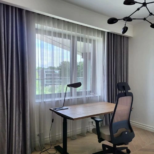 Home office blackout curtains in a sophisticated charcoal grey frame a bright window, layered over sheer white drapes.