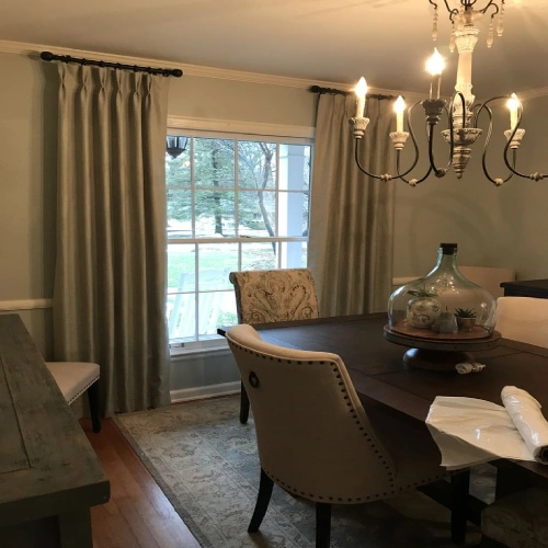 A light wood dining table and upholstered chairs positioned in front of French doors, framed by high-quality charcoal grey dining area blackout curtains