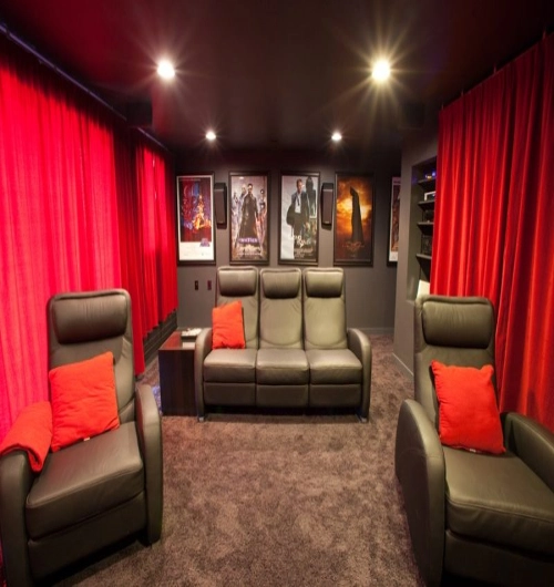 A luxurious private cinema room with vibrant red home theater blackout curtains framing grey leather recliner seating